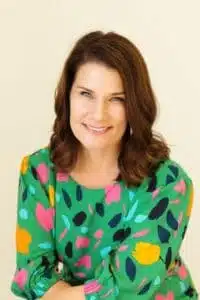 Woman smiling in colorful floral top.