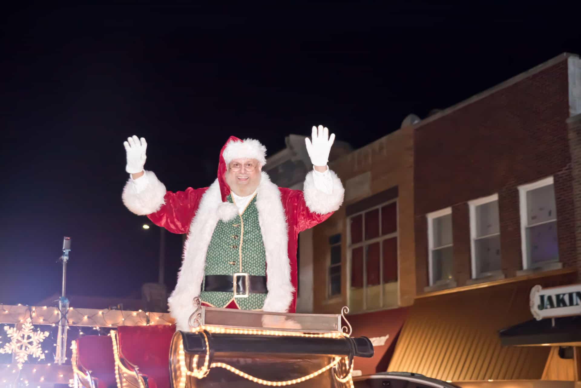 Person dressed as Santa Claus waving from parade float.