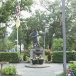 Soldier statue in park with American flags and flowers.