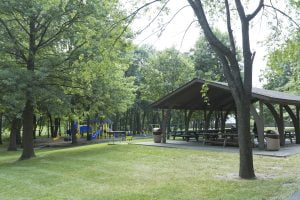 Park shelter and playground surrounded by green trees.