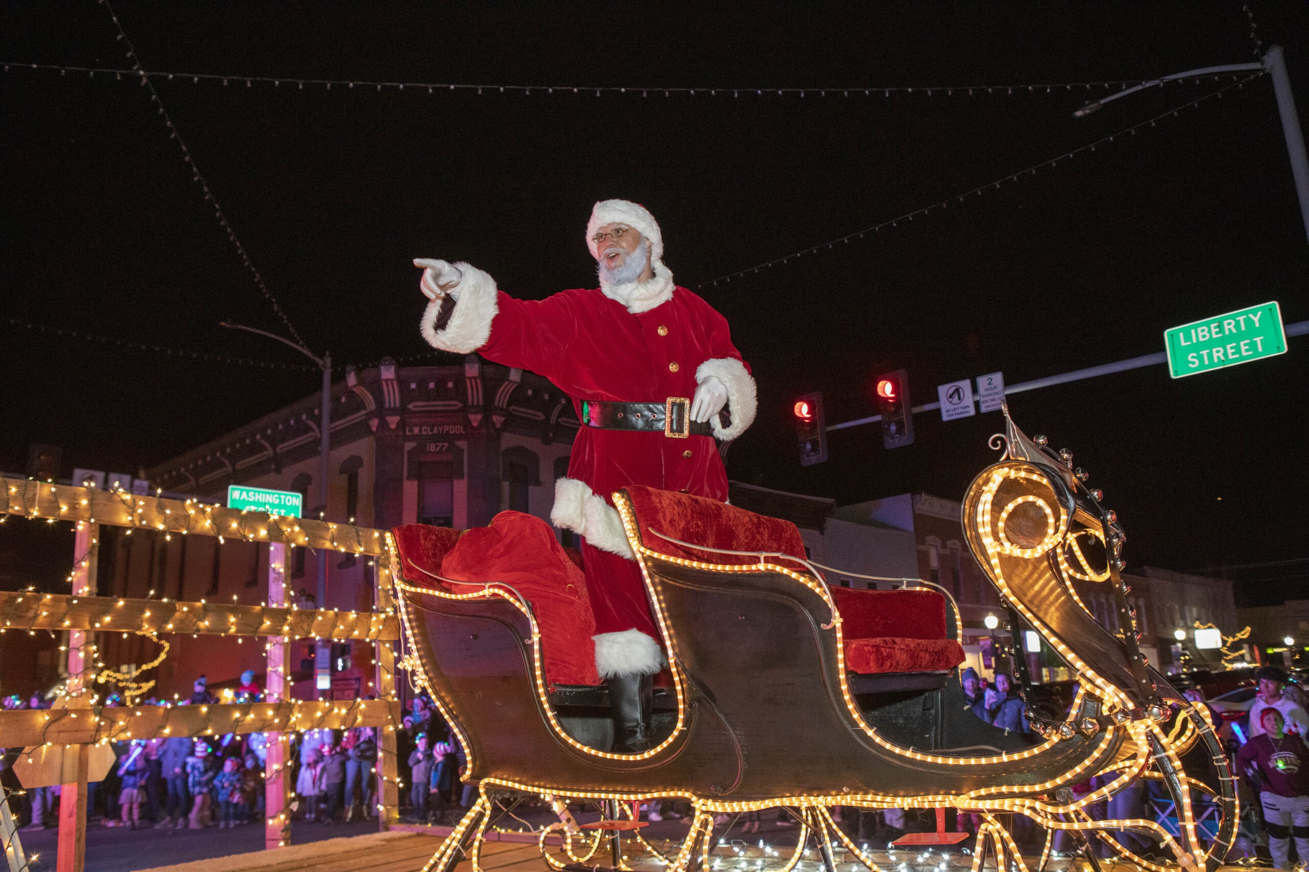 Santa Claus waving from illuminated sleigh during night parade.